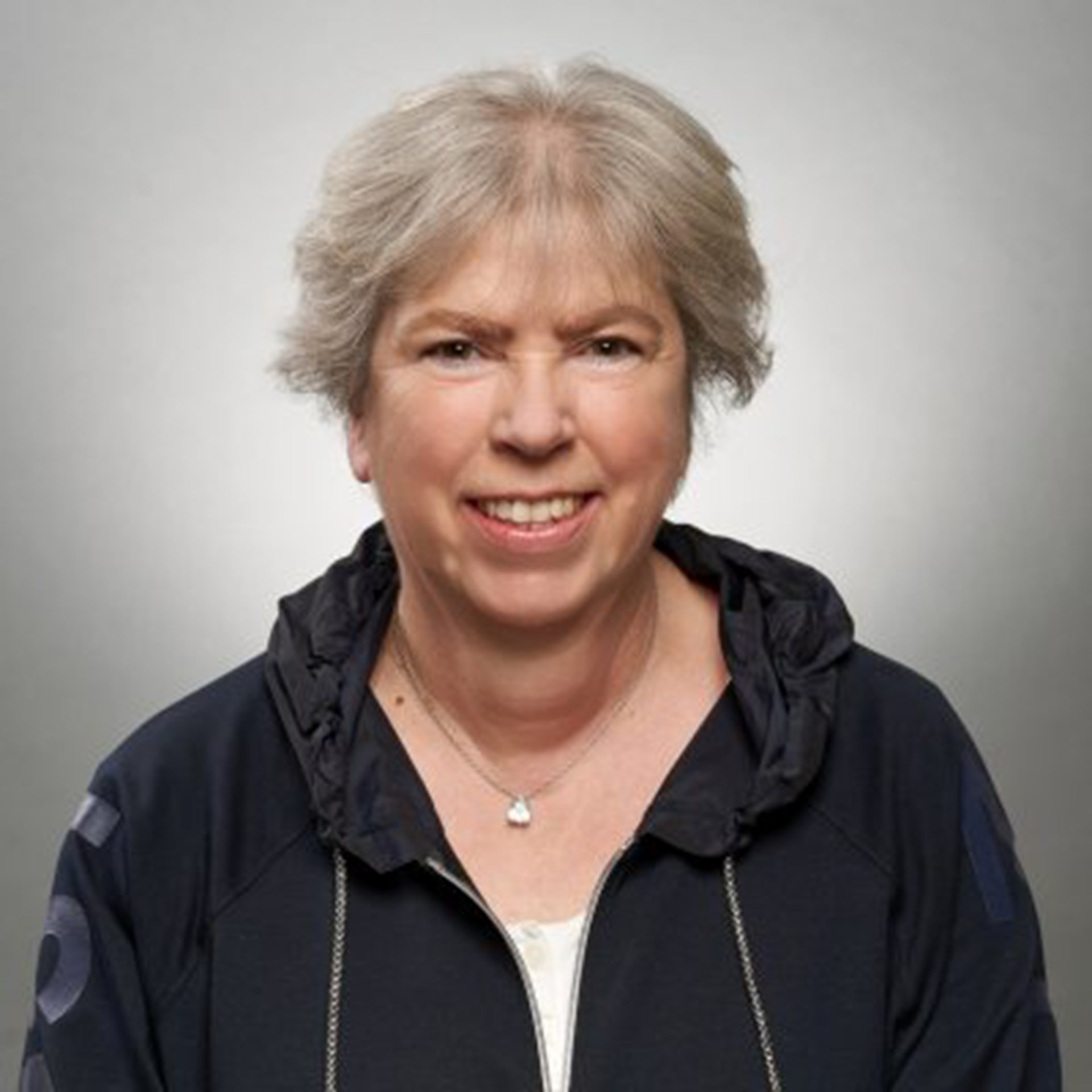 Lächelnde Frau mit grauen Haaren, die eine dunkle Kapuzenjacke und ein weißes Shirt trägt